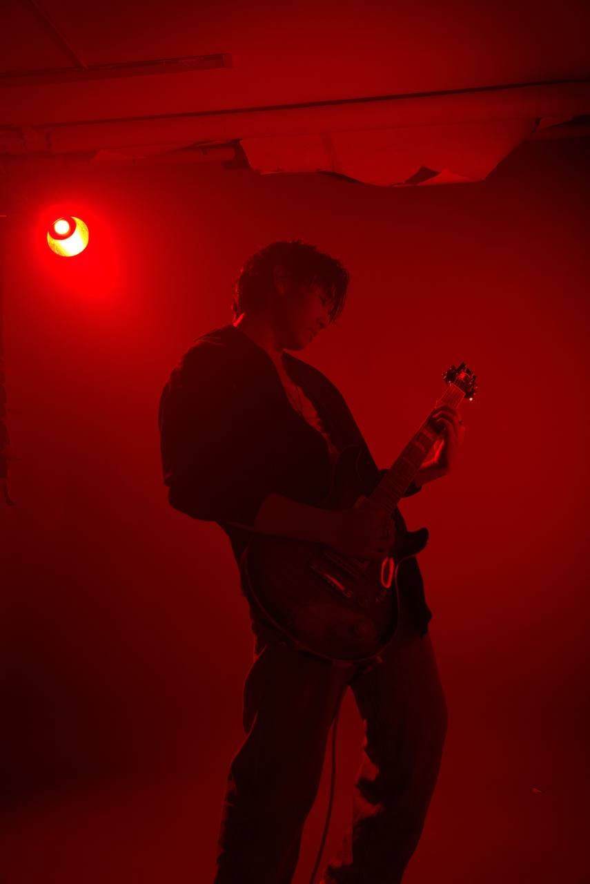 Alim playing electric guitar under a red stage light